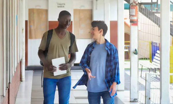 African boy meeting in the school hallway with his caucasian teenager schoolmate.