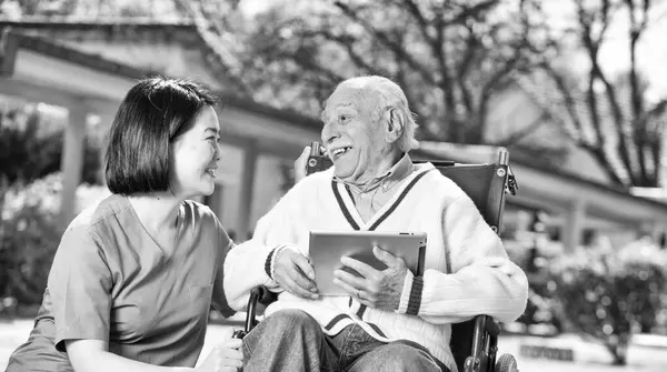 Nurse explaining use of tablet to elder people outdoor.
