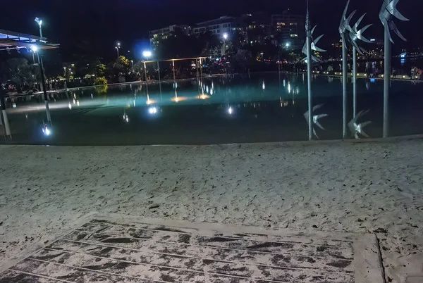 Tourists and locals walk at night along the Cairns city pool - Queensland, Australia.