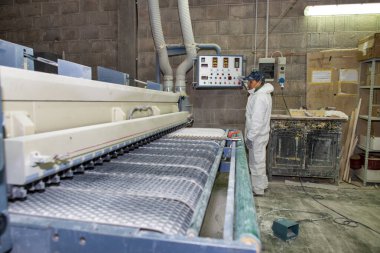 Bir erkek işçi ahşabı zımparalıyor ve vernikliyor..