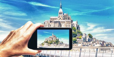 Akıllı telefonlu bir kadın Mont Saint Michel, Fransa 'nın fotoğrafını çekiyor. Turizm konsepti.