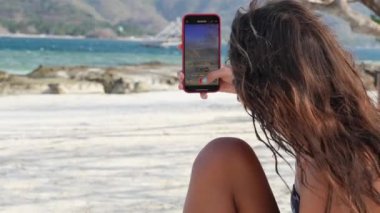 Bir kız güzel bir plajda akıllı telefonuyla video çekiyor..