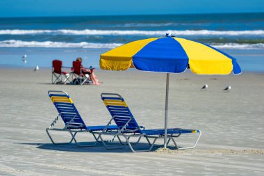 Florida, Daytona Sahili 'nde renkli plaj şemsiyesi ve sandalyeler.