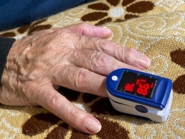 Yaşlı bir adam kan oksijenini tıbbi bir aletle ölçer..