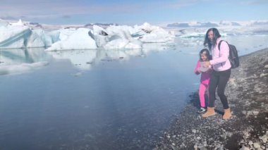 Anne ve kızı İzlanda 'daki Jokulsarlon Gölü' ne küçük buzdağları fırlatıyor. Yavaş çekim.