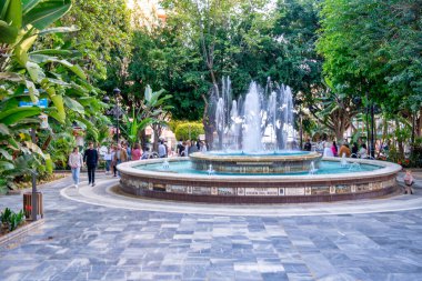 Marbella, İspanya - 5 Nisan 2023: İnsanlar şehir meydanında bir çeşme etrafında yürüyor.