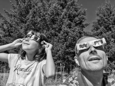 Baba ve kızı güneş tutulması sırasında bir kır parkında güneşe bakıyor. Aile aktivitesi..