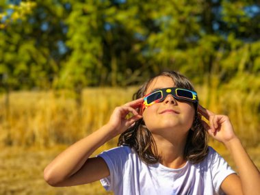 Güneş tutulması sırasında güneşe bakan genç bir kız. Şehir parkında, aile aktivitesi..