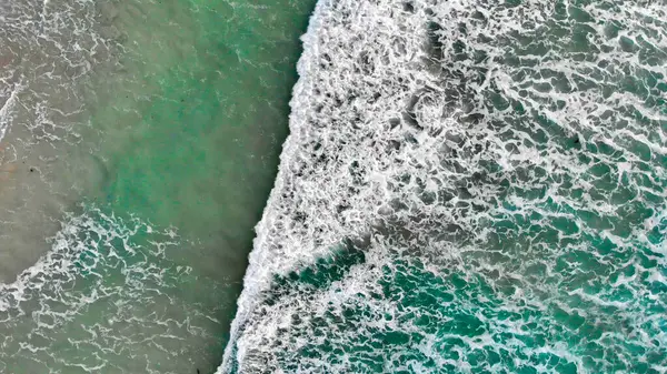 stock image Aerial downward view from above at waves crushing on a sandy beach.