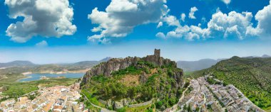 Panoramic aerial shot of Zahara de la Sierra showcasing its medieval castle and turquoise lake. clipart