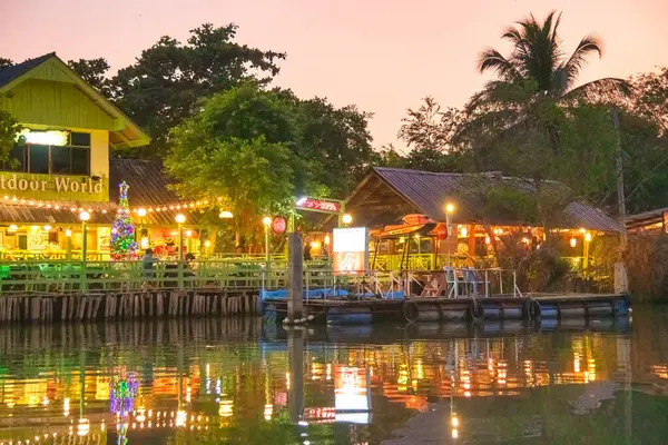 Amphawa Yüzen Pazarı 'nın gece görüşü. Nehir boyunca. Sudaki ışıkların yansımaları..