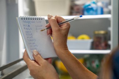 Organize kadın, buzdolabının içindekileri kontrol ederken market alışverişini de planlıyor..