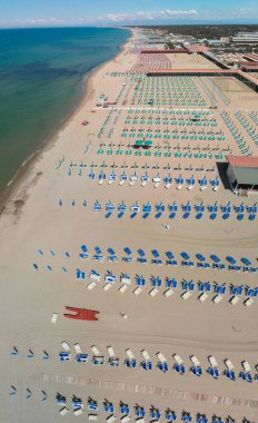 Sahildeki tesislerin tepeden tırnağa panoramik manzarası. Şemsiyeler ve güneşlikler sahil boyunca düzgünce dizilmiş..