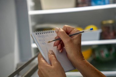 Kadın açık bir buzdolabının önünde dururken market listesi yazıyor..