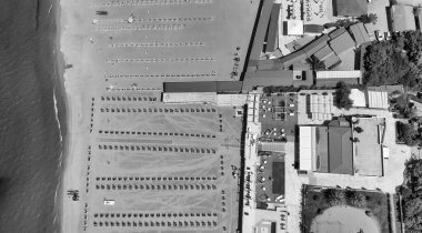 Yaz mevsiminde sıralı şemsiyeler ve güneşli yataklı bir sahil beldesinin havadan aşağı manzarası..