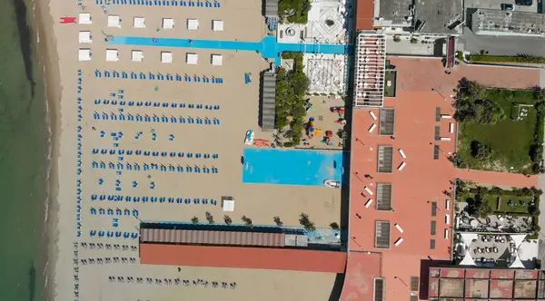 Yaz mevsiminde sıralı şemsiyeler ve güneşli yataklı bir sahil beldesinin havadan aşağı manzarası..