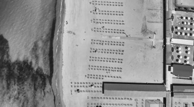 Yaz mevsiminde sıralı şemsiyeler ve güneşli yataklı bir sahil beldesinin havadan aşağı manzarası..