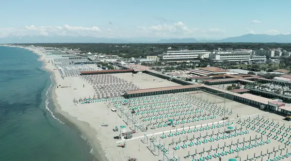 Yaz mevsiminde sıralı şemsiyeler ve güneşli yataklı bir sahil beldesinin havadan aşağı manzarası..