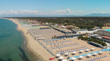 Yaz mevsiminde sıralı şemsiyeler ve güneşli yataklı bir sahil beldesinin havadan aşağı manzarası..