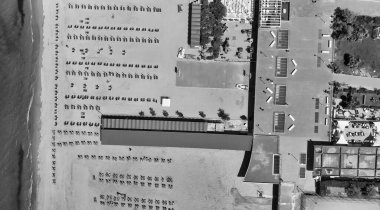 Yaz mevsiminde sıralı şemsiyeler ve güneşli yataklı bir sahil beldesinin havadan aşağı manzarası..