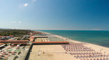 Yaz mevsiminde sıralı şemsiyeler ve güneşli yataklı bir sahil beldesinin havadan aşağı manzarası..