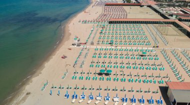 Yaz mevsiminde sıralı şemsiyeler ve güneşli yataklı bir sahil beldesinin havadan aşağı manzarası..