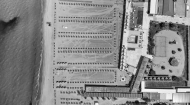 Canlı bir sahil kulübünün insansız hava aracı görüntüsü. Arka planda sıra sıra şemsiyeler ve berrak mavi deniz var..