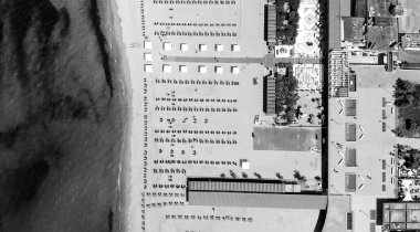 Yaz mevsiminde sıralı şemsiyeler ve güneşli yataklı bir sahil beldesinin havadan aşağı manzarası..