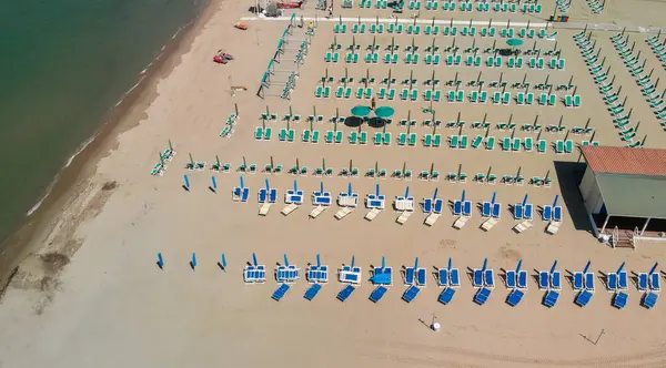 Yaz mevsiminde sıralı şemsiyeler ve güneşli yataklı bir sahil beldesinin havadan aşağı manzarası..