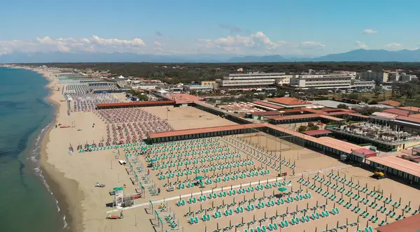 Yaz mevsiminde sıralı şemsiyeler ve güneşli yataklı bir sahil beldesinin havadan aşağı manzarası..