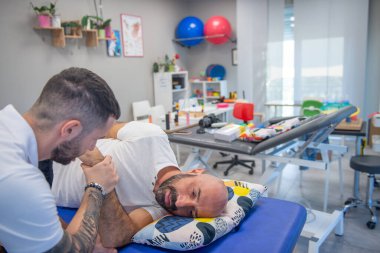 Osteopat, bir erkeğin omzuna kanepede fizyoterapi uyguluyor..