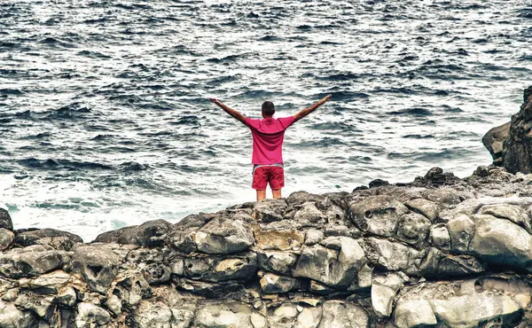 Man relaxing and embracing nature standing on the rocks above the ocean. Holiday concept
