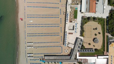 Yaz mevsiminde sıralı şemsiyeler ve güneşli yataklı bir sahil beldesinin havadan aşağı manzarası..