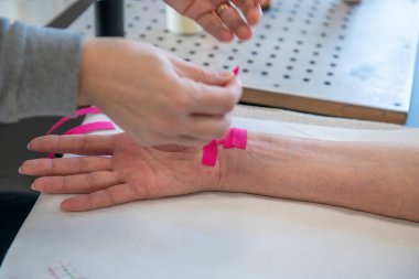 Fizyoterapist, genç bir kadının bileğine ağrı kesici bant yapıştırıyor.. 