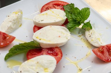 Taze Caprese aperatifleri dilimlenmiş domatesler, kremalı mozarella ve kırsal bir tabakta yeşil fesleğen..
