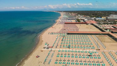 Yaz mevsiminde sıralı şemsiyeler ve güneşli yataklı bir sahil beldesinin havadan aşağı manzarası..
