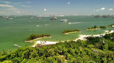 Arka planda tatil köyleri, palmiye ağaçları ve kentsel ufuk çizgisi olan Sentosa Adası manzaralı güneşli bir gün..