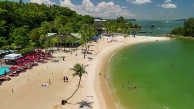 Singapur 'daki Sentosa Sahili' nin havadan görünüşü kumlu kıyıları, turkuaz suyu ve plaja gidenleri gösteriyor..
