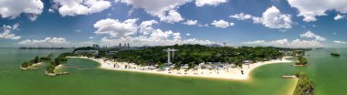 Sentosa Adası Singapur 'un kumlu plajları, temalı parkları ve arka planda şehir silueti olan insansız hava aracı görüntüsü.