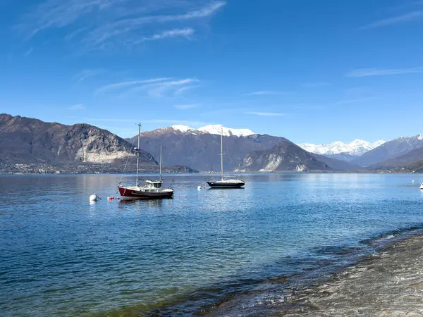Maggiore Gölü 'ne demirli yelkenliler ve arka planda karla kaplı Alpler. İtalya, Verbania 'da huzurlu bir bahar sahnesi çekildi.