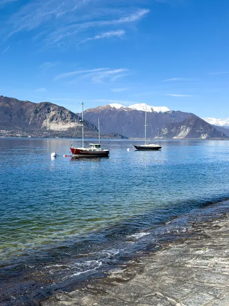 Maggiore Gölü 'ne demirli yelkenliler ve arka planda karla kaplı Alpler. İtalya, Verbania 'da huzurlu bir bahar sahnesi çekildi.