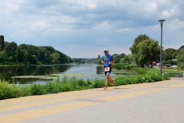 BILA TSERKVA, UKRAINE - 23 Temmuz 2023 tarihinde Ukrayna 'nın Bila Tserkva kentinde gerçekleştirilen ulusal triatlon müsabakasında Ros nehri kenarındaki toprak dolgusu üzerinde koşan atlet.