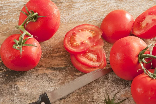 新鲜成熟的红色桁架西红柿片与锯齿状厨房刀在一个真实的锯木板上 — 图库照片