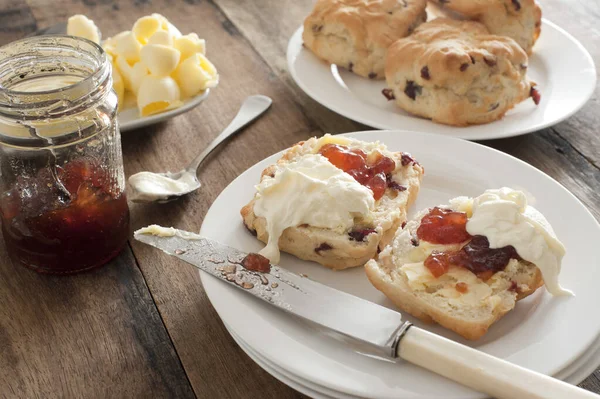 新鲜烘焙的水果饼 配上果酱和奶油 放在茶壶 卷曲的黄油和饼干盘中 围坐在桌子旁 免版税图库照片