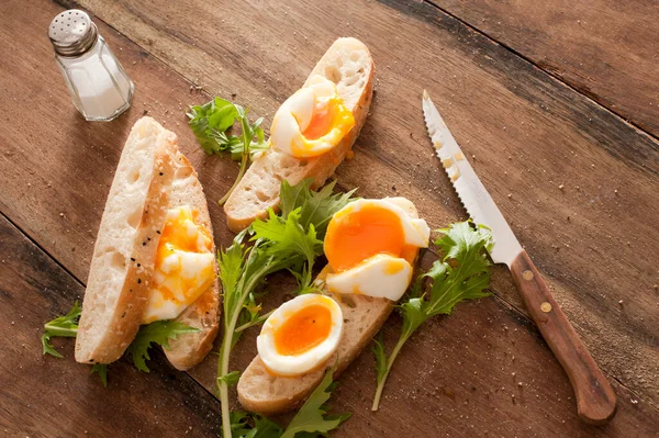 焼き立てのサラダグリーンのバゲットにゆで卵のおいしい朝食ナイフで木製のテーブルの上に高い角度を見た ストック写真