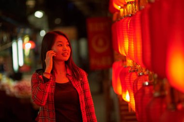 Çin Yeni Yılı yakınlarında cep telefonuyla konuşan bir kadın. Geceleri kırmızı fenerler..