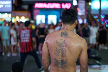 PHUKET, THAILAND - 25 Nisan 2023: dövme geceleyin Patong Beach Bangla Walking Street 'te bir adamın arkasında görüldüğü gibi. 