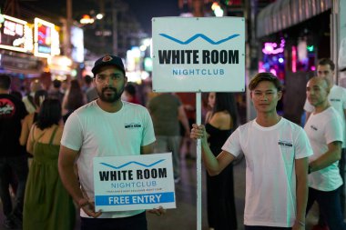 PHUKET, THAILAND - APRIL 25, 2023: two men with ad posters on Patong Beach Bangla Walking Street in the night. clipart