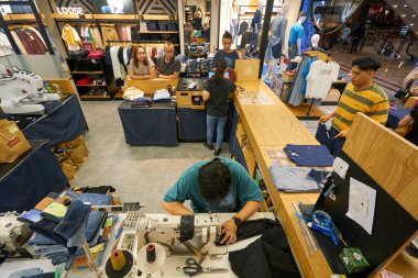 KUALA LUMPUR, MALAYSIA - CIRCA MAYIS, 2023: Adam Kuala Lumpur 'daki Suria KLCC alışveriş merkezindeki Levi' nin dükkanında Juki dikiş makinesinde dikiş dikiyor.