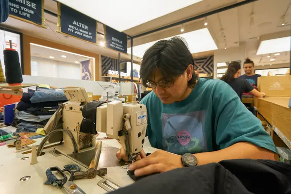 Stock image KUALA LUMPUR, MALAYSIA - CIRCA MAY, 2023: indoor portrait of man sew at Juki sewing machine in Levi's store at Suria KLCC shopping mall in Kuala Lumpur.